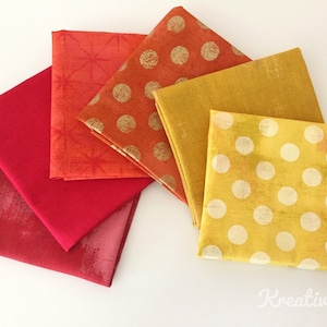 Könnte beinhalten: Eine Sammlung farbenfroher Stoffquadrate in Rot-, Orange- und Gelbtönen. Einige Quadrate weisen Muster wie Polka-Punkte und Sternausbrüche auf, während andere unifarben sind. Der Stoff ist fächerförmig angeordnet und zeigt die Vielfalt der Texturen und Farbtöne.