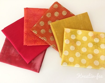 Könnte beinhalten: Eine Sammlung farbenfroher Stoffquadrate in Rot-, Orange- und Gelbtönen. Einige Quadrate weisen Muster wie Polka-Punkte und Sternausbrüche auf, während andere unifarben sind. Der Stoff ist fächerförmig angeordnet und zeigt die Vielfalt der Texturen und Farbtöne.
