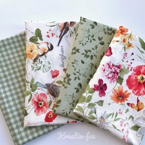 May include: Four folded fabric pieces with floral and botanical patterns. One piece has a green gingham pattern. The other three feature flowers, birds, and foliage in shades of red, orange, green, and white. The word "everything" is printed on one.