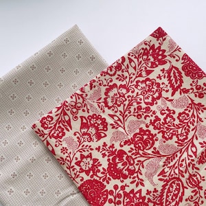 May include: Two folded fabric pieces. One is beige with a repeating pattern of small brown floral shapes. The other is beige with a vibrant red floral design. The fabrics are likely for sewing or crafting.
