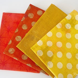 Puede incluir: Cuatro servilletas de tela plegadas en tonos rojos, naranjas y amarillos. Las servilletas tienen varios patrones, incluyendo explosiones de estrellas y lunares dorados. Las servilletas son probablemente para la decoración del hogar o para cenar.