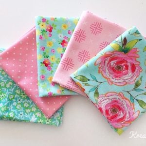 Könnte beinhalten: Eine Sammlung gefalteter Stoffquadrate in verschiedenen floralen und gemusterten Designs. Die Stoffe weisen Rosa-, Türkis- und Grüntöne mit Blumen-, Tupfen- und geometrischen Mustern auf. Die Stoffquadrate sind fächerförmig angeordnet.