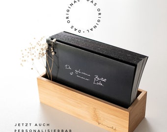 Könnte beinhalten: Ein Satz schwarzer Karten mit weißem Text in einer Holzkiste. Der Text auf den Karten lautet "Die gelbe ist immer zuerst da." Die Kiste trägt den Text "Das Original" in einem Kreis und "yourwald" ist unten eingraviert. Der Text "JETZT AUCH PERSONALISIERBAR" ist unter der Kiste gedruckt.