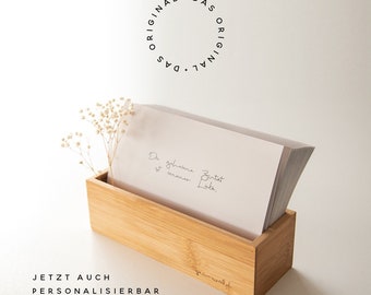 May include: A wooden card holder with a stack of cards inside. The cards have handwritten text that reads "The future is always bright." The holder is on a white surface with a small bouquet of white flowers.
