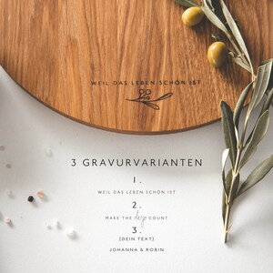 May include: A round wooden serving board with engraved text and a decorative olive branch. The text includes "WEIL DAS LEBEN SCHON IST", "Make the days count", and space for custom text. Olives and olive branches are arranged around the board.