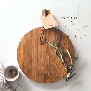 May include: A round wooden cutting board, 29 cm in diameter and 39.5 cm long, with a handle and a tag. The board has the text "MAKE THE MOMENT COUNT". An olive branch and a small bowl of salt are also present.