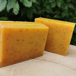 May include: Two bars of yellow soap with poppy seeds. The soap is on a wooden surface.
