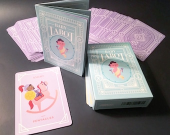 May include: A set of Baby Tarot cards with a light blue and white design. The cards feature illustrations of babies in various poses. The box is light blue with the words "Baby Tarot" in white. A single card is shown with a knight riding a rocking horse.