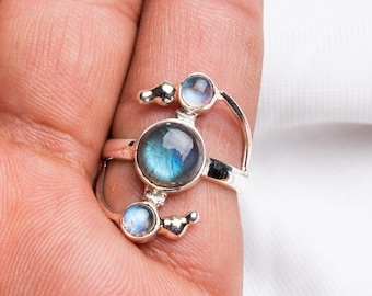 May include: A silver ring with three blue and white gemstone accents. The ring has a unique design with a curved band and a large center stone.