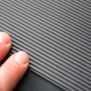 Op de afbeelding: Close-up van een grijze, getextureerde rubberen mat met parallelle ribbels. De mat heeft een licht ruw oppervlak.