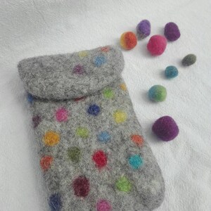 Könnte beinhalten: Eine graue Filz-Handyhülle mit einem bunten Punkte-Muster. Die Hülle liegt auf einer weißen Oberfläche mit mehreren kleinen, bunten Filzkugeln, die um sie herum verstreut sind.