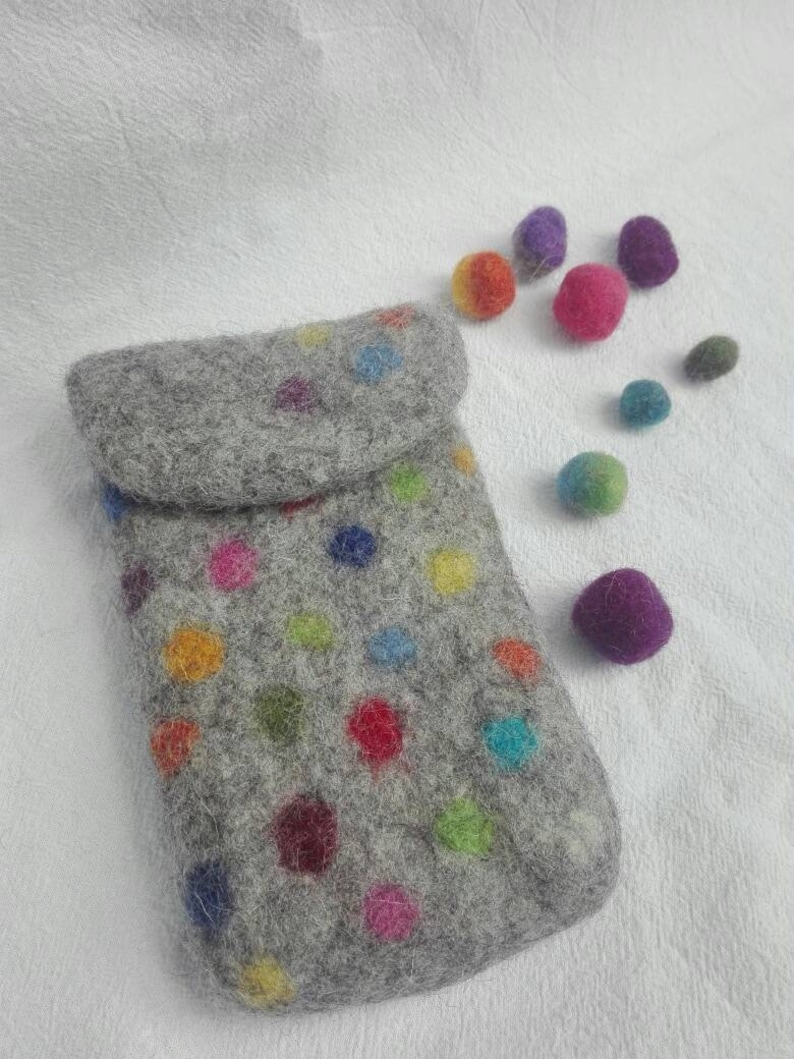 May include: A gray felt phone case with a colorful polka dot pattern. The case is lying on a white surface with several small, colorful felt balls scattered around it.