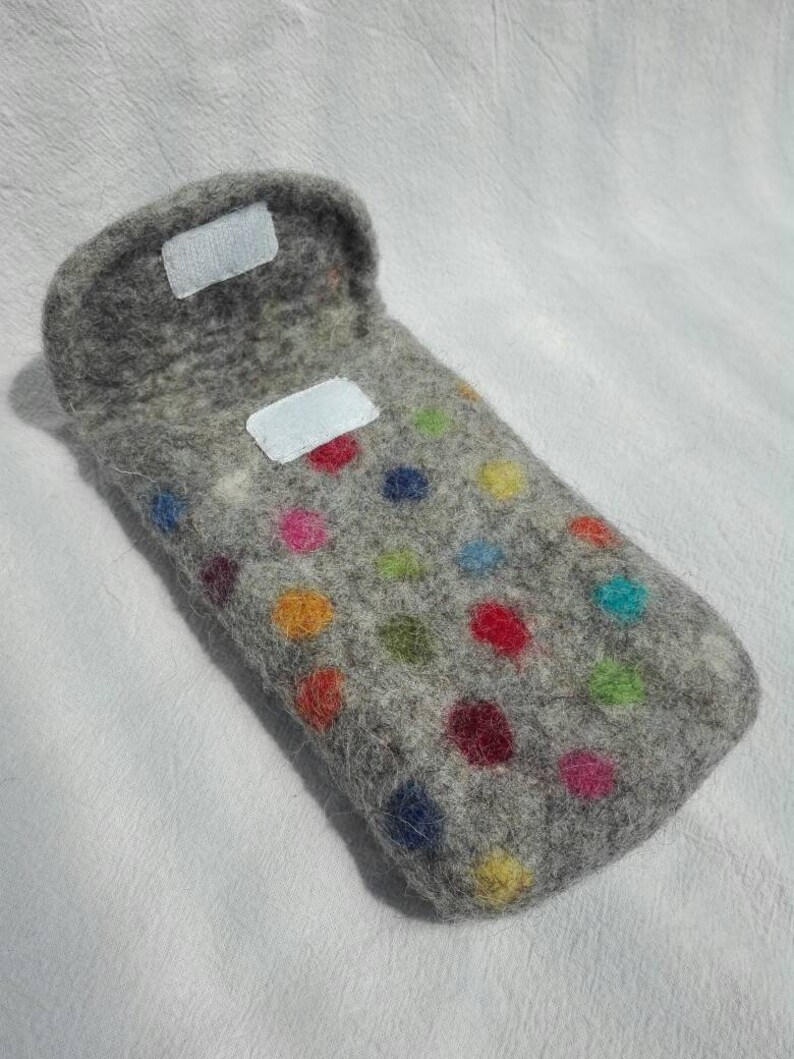 May include: A gray felt phone case with colorful polka dots. The case has a flap that closes with a velcro closure.
