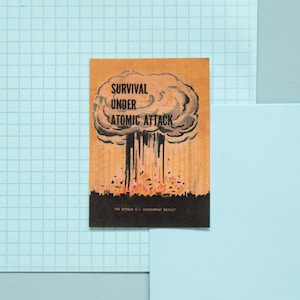 May include: A vintage-style illustration of a mushroom cloud with the text "SURVIVAL UNDER ATOMIC ATTACK" and "THE OFFICIAL U.S. GOVERNMENT BOOKLET" printed below.