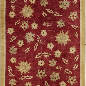 Puede incluir: Una alfombra roja con un patrón floral en tonos dorados y verdes. La alfombra presenta un diseño repetitivo de flores y hojas estilizadas.