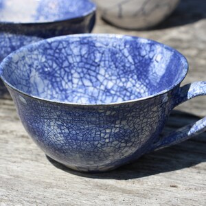 Puede incluir: Una taza de t&eacute; de cer&aacute;mica azul y blanca con un esmalte craquelado. La taza tiene un asa y est&aacute; sentada sobre una superficie de madera.