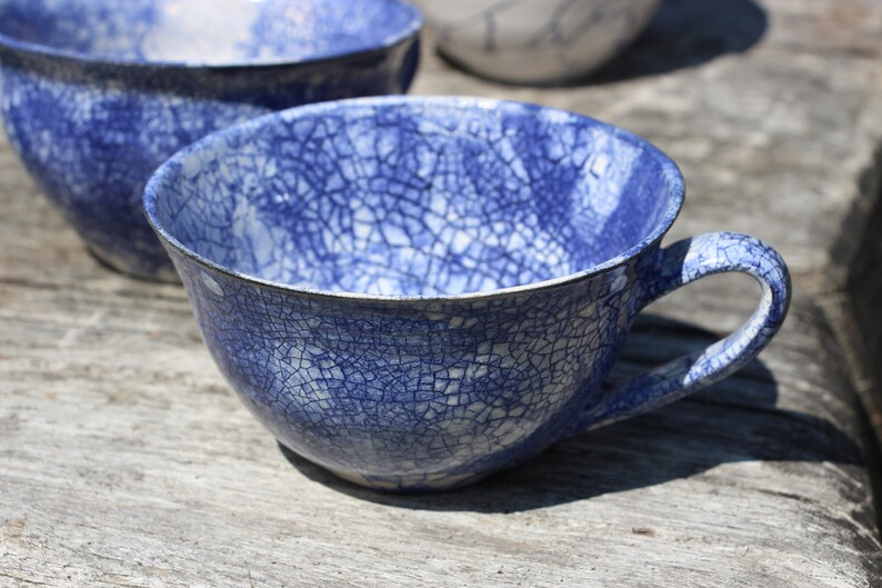 Puede incluir: Una taza de t&eacute; de cer&aacute;mica azul y blanca con un esmalte craquelado. La taza tiene un asa y est&aacute; sentada sobre una superficie de madera.