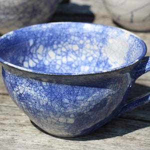 Puede incluir: Una taza de t&eacute; de cer&aacute;mica azul y blanca con un esmalte craquelado. La taza tiene una forma redondeada y un asa.