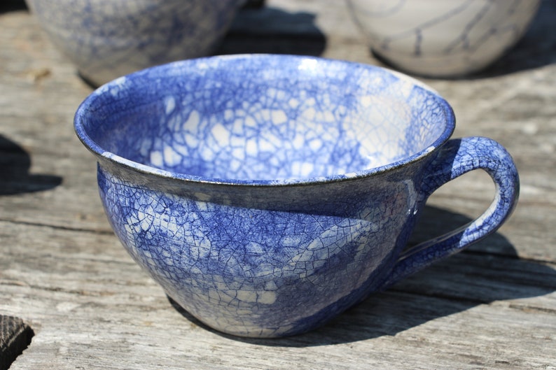 Puede incluir: Una taza de t&eacute; de cer&aacute;mica azul y blanca con un esmalte craquelado. La taza tiene una forma redondeada y un asa.