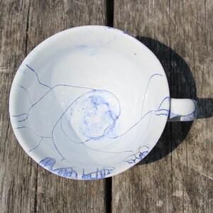 Puede incluir: Una taza de t&eacute; de cer&aacute;mica blanca con un dise&ntilde;o de remolino azul y blanco. La taza tiene un asa y est&aacute; sentada sobre una superficie de madera.