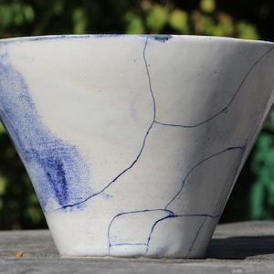 Puede incluir: Un cuenco de cerámica blanca con un esmalte craquelado azul y blanco. El cuenco tiene forma de cono y un borde ancho.