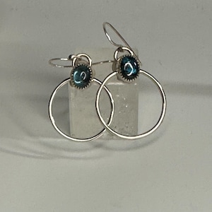 May include: A pair of silver hoop earrings with a blue gemstone in each hoop.