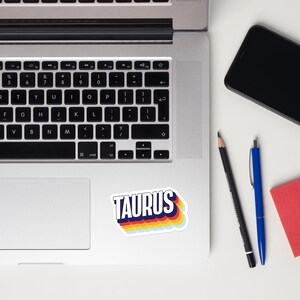 Puede incluir: Un ordenador portátil con un teclado y una pegatina que dice "TAURUS" en colores arcoíris.