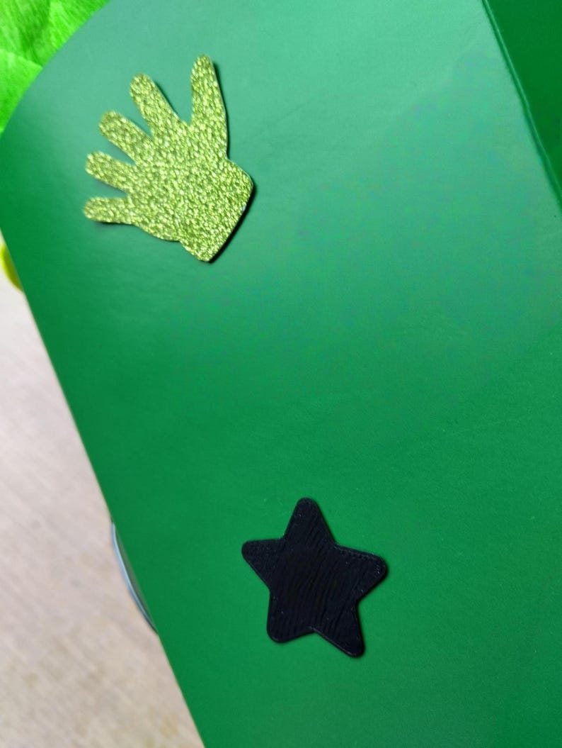 Peut inclure: Une surface vert vif avec une d&eacute;coupe en forme de main verte scintillante et une d&eacute;coupe en forme d'&eacute;toile noire. La d&eacute;coupe de la main a un aspect textur&eacute; et scintillant. L'&eacute;toile est noire unie.