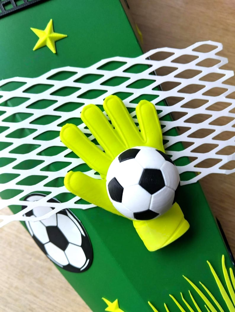 Peut inclure: Une bo&icirc;te d&eacute;corative verte sur le th&egrave;me du football. Elle pr&eacute;sente un gant de gardien de but jaune tenant un ballon de football noir et blanc, un filet blanc et une &eacute;toile jaune. Un graphisme de ballon de football est &eacute;galement visible.
