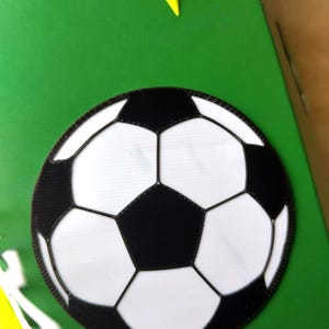 Peut inclure: Un &eacute;cusson de ballon de football avec des pentagones et hexagones noirs et blancs, sur fond vert. Une &eacute;toile jaune est dans le coin sup&eacute;rieur. L'&eacute;cusson est probablement destin&eacute; &agrave; un projet d'artisanat sur le th&egrave;me du sport.