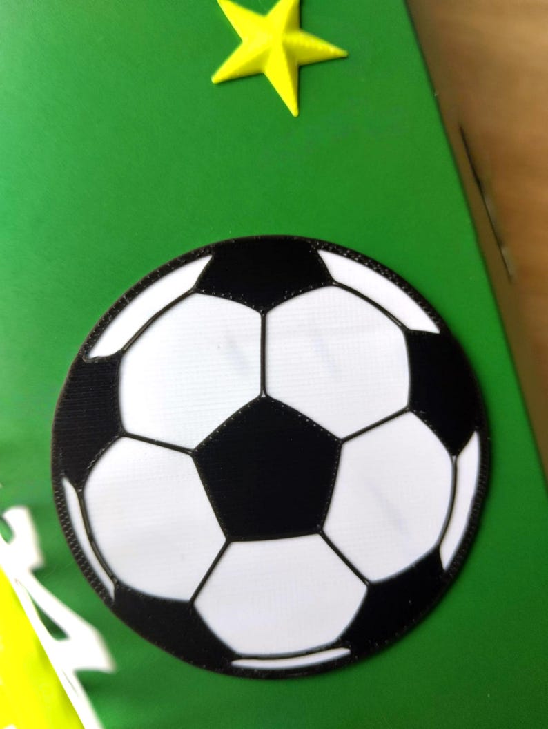 Peut inclure: Un &eacute;cusson de ballon de football avec des pentagones et hexagones noirs et blancs, sur fond vert. Une &eacute;toile jaune est dans le coin sup&eacute;rieur. L'&eacute;cusson est probablement destin&eacute; &agrave; un projet d'artisanat sur le th&egrave;me du sport.