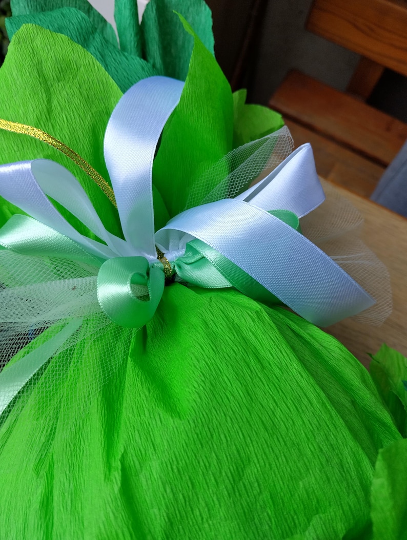 Peut inclure: Gros plan sur un cadeau envelopp&eacute; dans du papier cr&eacute;pon vert vif, orn&eacute; de rubans de satin bleu clair et vert. Une ficelle dor&eacute;e et un filet blanc ajoutent des d&eacute;tails &agrave; la pr&eacute;sentation. Le cadeau est probablement pour une occasion sp&eacute;ciale.
