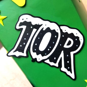 Peut inclure: Gros plan sur une surface verte avec un graphisme noir et blanc indiquant "10R". Le graphisme a une bordure blanche et des points blancs. Des accents en forme d'&eacute;toiles jaunes sont visibles dans les coins.