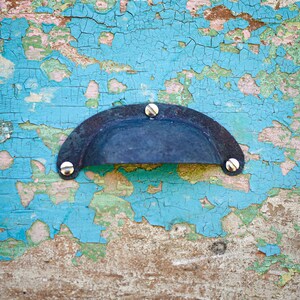 May include: A black metal door handle with silver screws, mounted on a blue and green painted wooden surface with peeling paint.