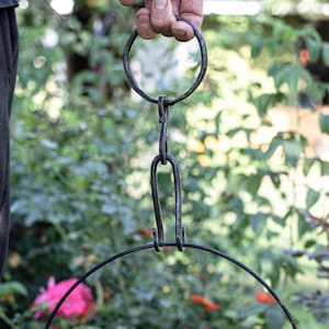 Könnte beinhalten: Ein schwarzer Metall-Haken zum Aufhängen mit einem Ring oben und einem gebogenen Haken unten. Der Haken ist an einer Kette befestigt.