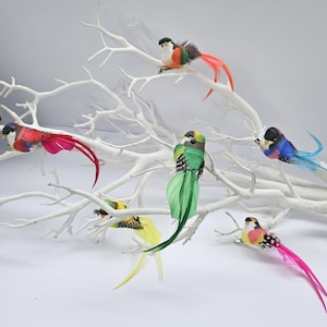 May include: Six colourful feathered birds with wire legs are perched on a white branch. The birds are decorated with various colours, including red, green, blue, yellow, and pink.