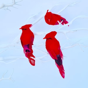 Könnte beinhalten: Drei rote Kardinalvögel mit schwarzen Akzenten an den Flügeln sitzen auf einem weißen Ast. Die Vögel sind aus Federn gefertigt und haben ein realistisches Aussehen.