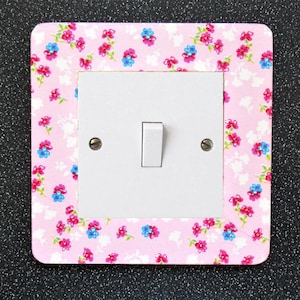 May include: A white light switch with a pink floral patterned cover. The cover has a pink background with small blue and pink flowers.