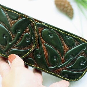 May include: A green leather pencil case with a floral design and yellow stitching.