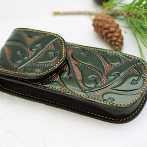 May include: A green leather case with a floral design and yellow stitching. The case is closed and has a flap.