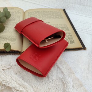 open red leather glasses case with your glasses inside and with the talabar logo engraved on it on an old open book