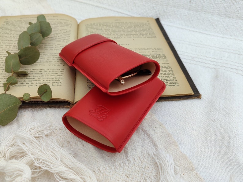 open red leather glasses case with your glasses inside and with the talabar logo engraved on it on an old open book