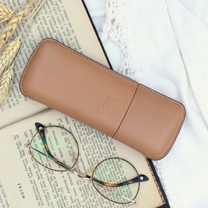 beige leather glasses case with talabar logo engraved on an old open book