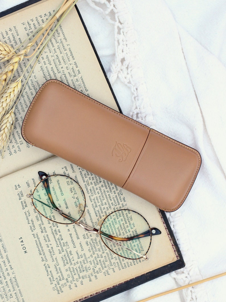 beige leather glasses case with talabar logo engraved on an old open book