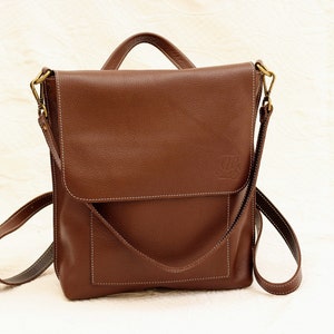 Peut inclure: Un sac à bandoulière en cuir marron avec une fermeture à rabat et une seule sangle. Le sac a une petite poche sur le devant et un logo en relief sur le rabat.