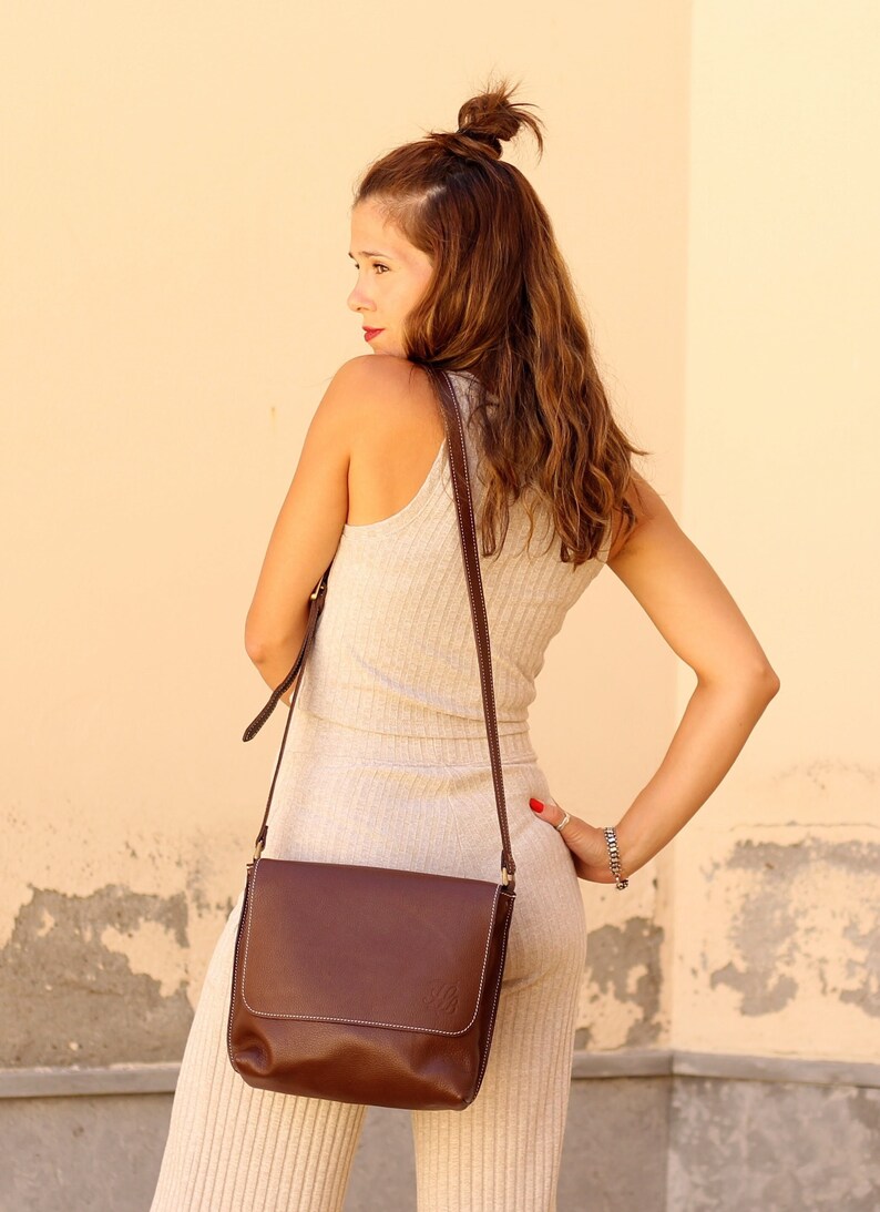 May include: A woman wearing a beige ribbed jumpsuit with a brown leather shoulder bag. The bag has a long strap and a flap closure.
