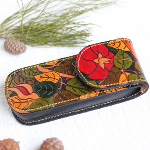 Op de afbeelding: Een bloemenpatroon lederen bril etui met een rood bloemenontwerp. De etui is gesloten en heeft een gele stiksel rond de randen.