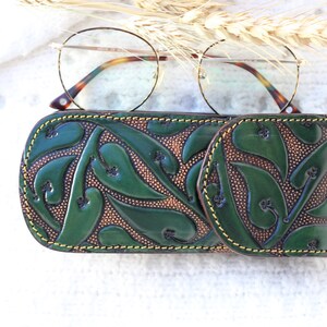 May include: A green leather glasses case with a floral pattern. The case has a yellow stitch around the edges.
