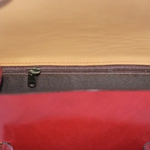 May include: The inside of a red leather handbag with a brown fabric lining and a zipper closure.