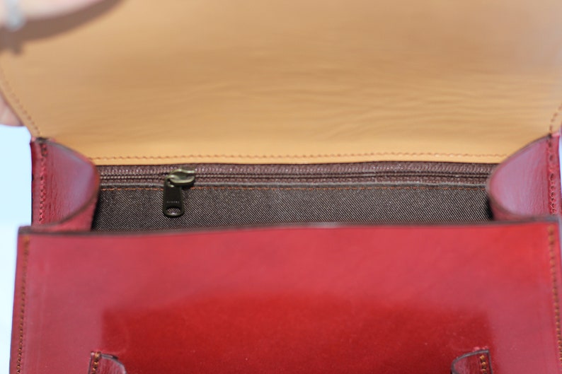 May include: The inside of a red leather handbag with a brown fabric lining and a zipper closure.